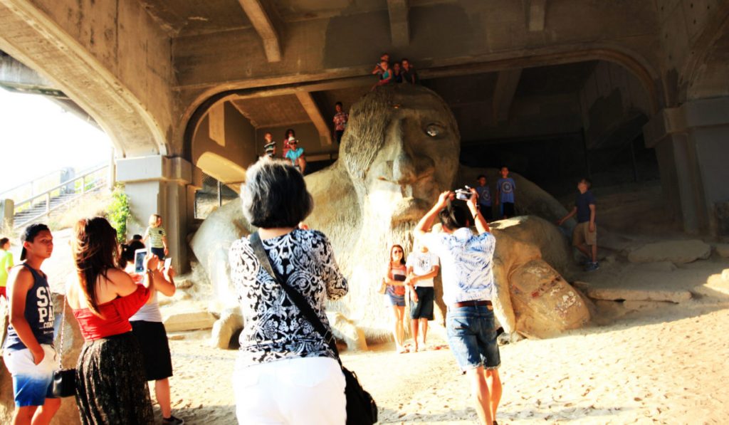 A group of people surrounding the Fremont troll, climbing it and taking photos