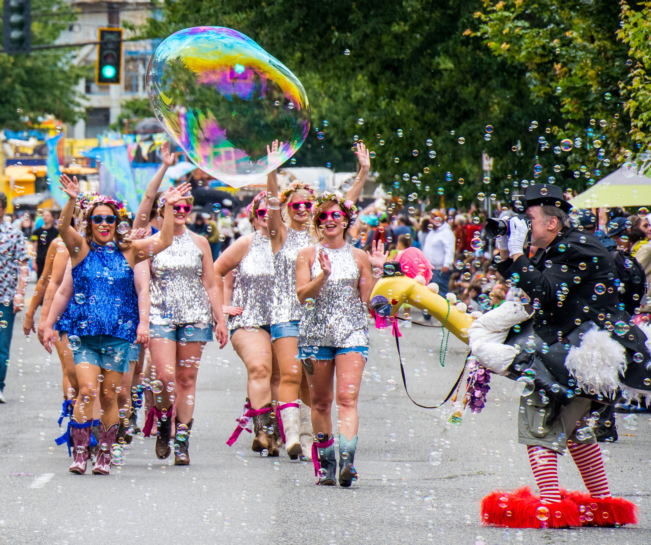 A group of people in glittery shirts at the Fremont Solstice Parade with bubbles flying everywhere. There is a person in a costume taking photos.