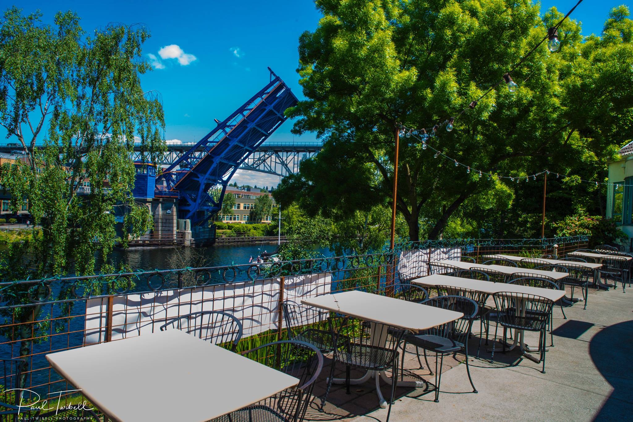 outdoor patio with view of trees, a waterway and an open bascule bridge