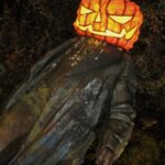 Bronze statue of Lenin at night with a giant lit pumpkin on his head.