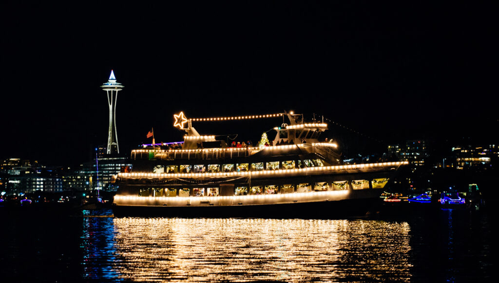 Motor boat decorated for Christmas in front of the Seattle Space Needle at night.