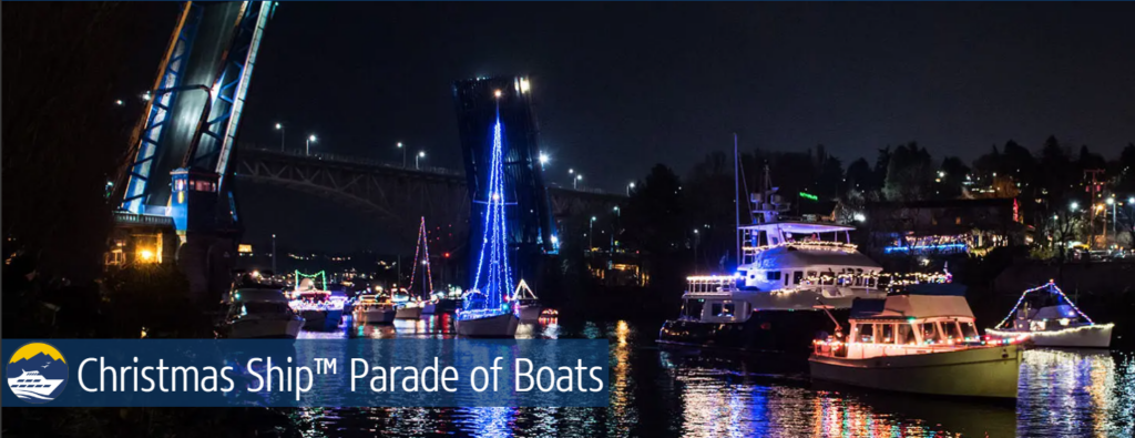 Brightly lit boats at night moving in a parade along the shoreline.